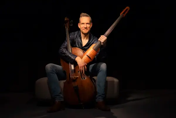 Orquesta sinfónica tocando en un auditorio, con un violonchelista solista en primer plano y el director al frente.
